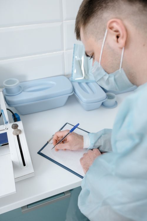 Free A medical professional wearing a mask writes notes on a clipboard in a hospital setting. Stock Photo