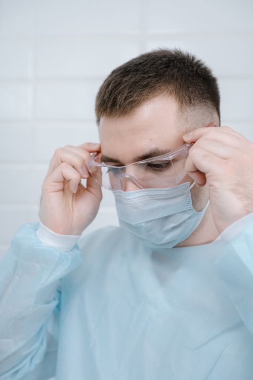 Free Male healthcare worker adjusting protective goggles and face mask for safety measures. Stock Photo