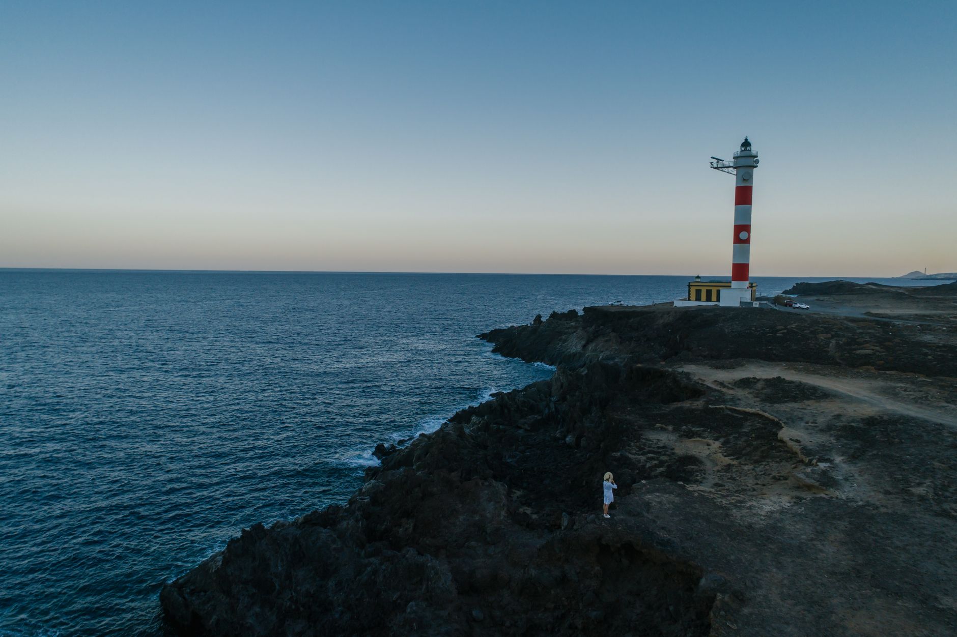 Dramatic view of a red and white lighthouse on a rugged coastal cliff with a vast ocean view.