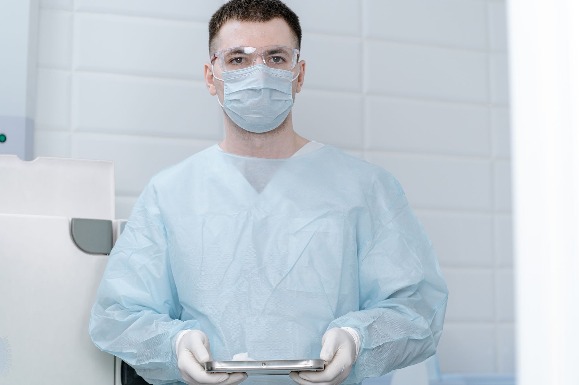 Doctor in operating gown with mask holding medical instrument in clinic.