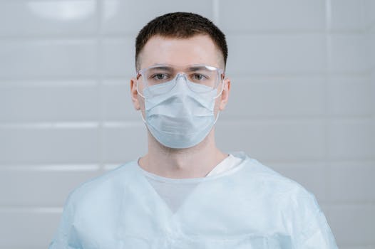 A male healthcare worker wearing a surgical mask and protective eyewear.