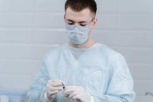 Doctor wearing Face Mask and a Scrub Suit holding a Syringe 