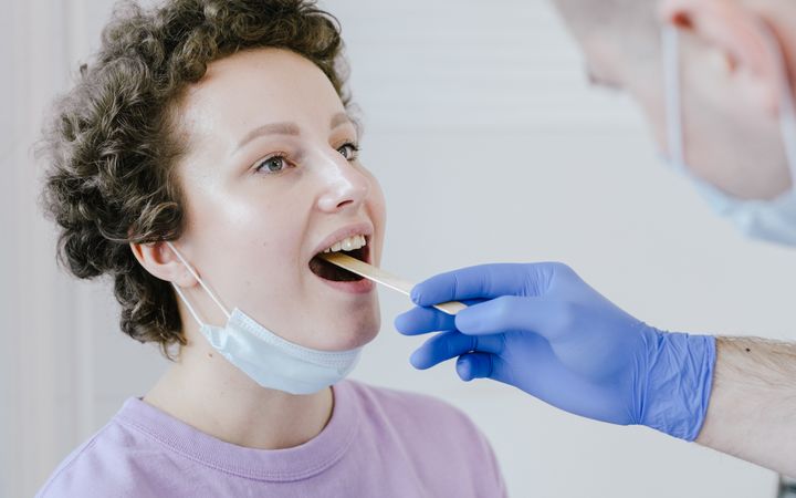 Healthcare professional swabbing a woman's throat for COVID-19 test indoors.