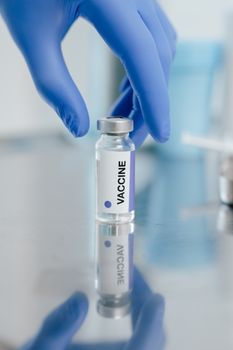 Gloved hand holding vaccine vial in laboratory setting, showcasing COVID-19 preparedness.