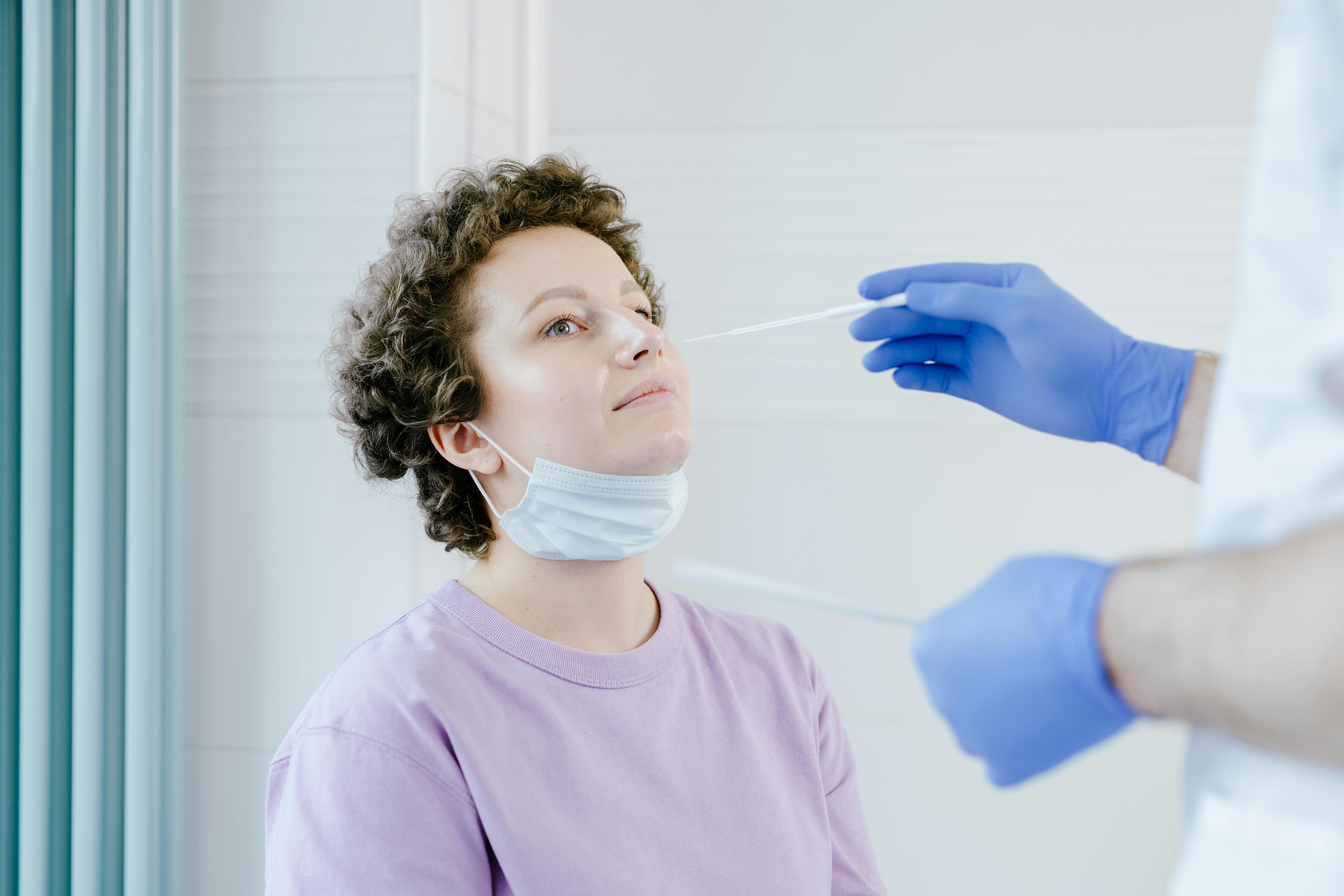 Healthcare worker administering a COVID-19 swab test to a patient indoors.