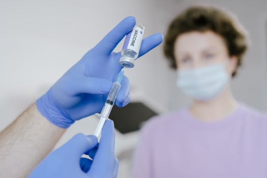 Close-up of healthcare professional in blue gloves filling a syringe with vaccine, patient in the background.