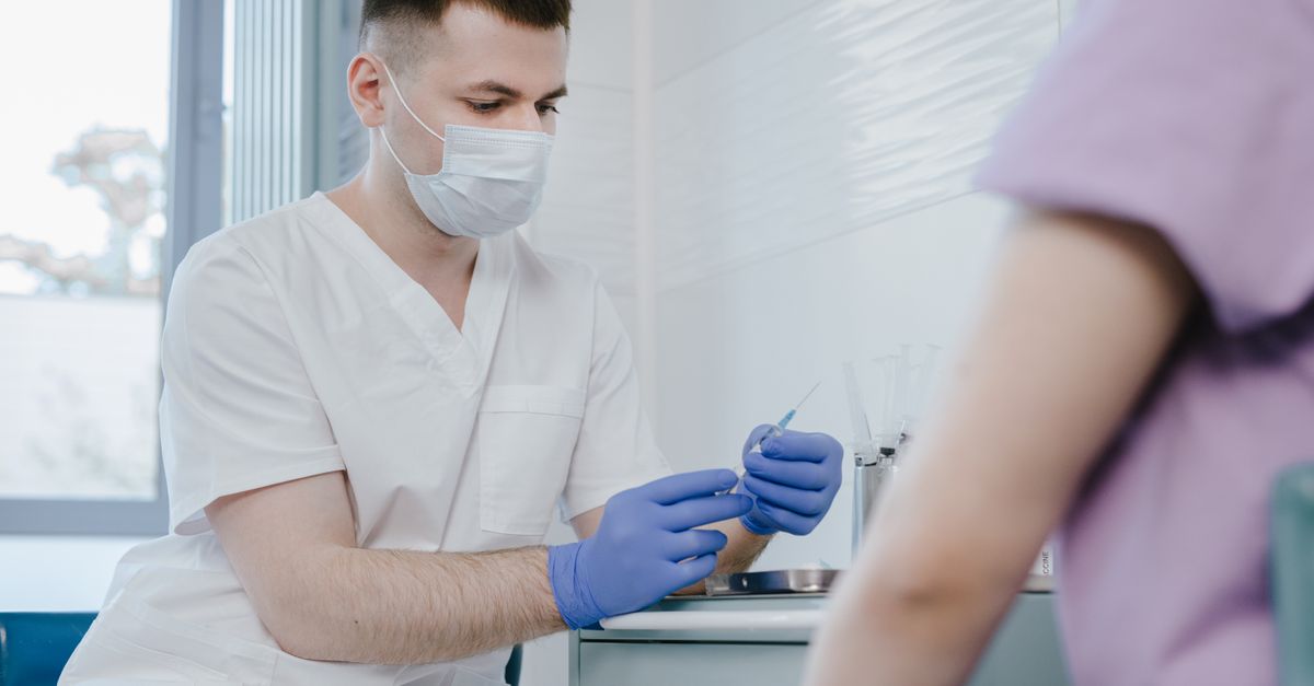 Healthcare worker in protective gear preparing a syringe for vaccination indoors.