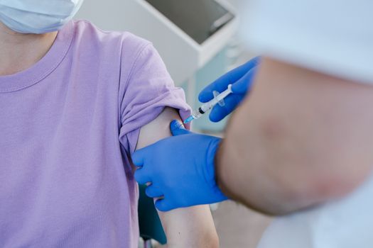 Close-up of a healthcare worker giving a vaccine shot to a patient wearing a purple shirt.