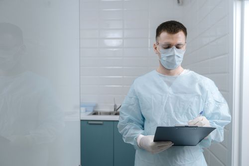 Free A doctor wearing a mask and goggles writes notes in a clinical setting, displaying medical professionalism. Stock Photo