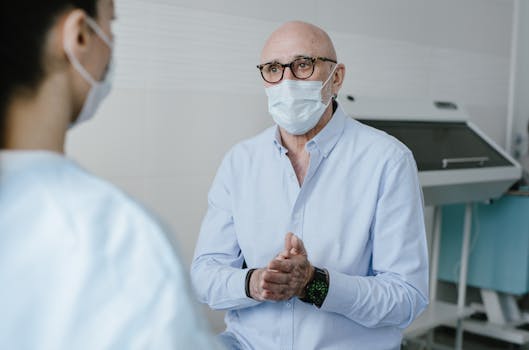 Masked bald doctor in conversation with patient, focus on new normal healthcare.