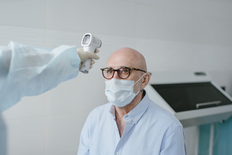 A Person Taking The Temperature Of A Man Wearing A Face Mask