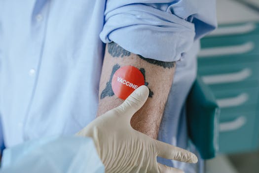 A healthcare professional applies a vaccine sticker on a tattooed arm in a medical environment.