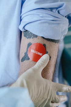 A gloved hand places a vaccine sticker on a tattooed arm, symbolizing vaccination.
