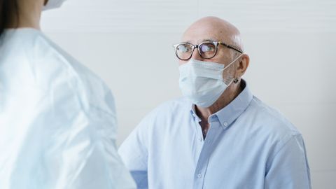 A medical professional discusses health with a senior patient, both wearing face masks for safety.