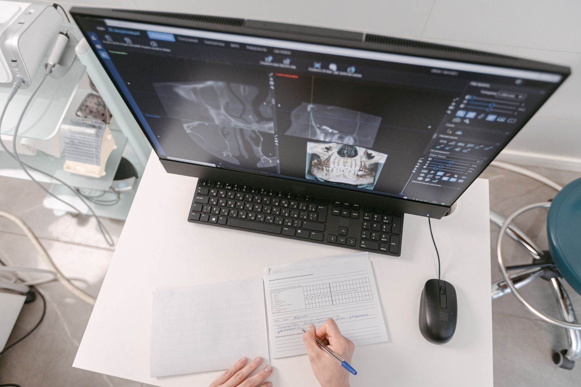 Radiologist analyzing X-ray scans on a computer monitor while taking notes. Medical documents visible.