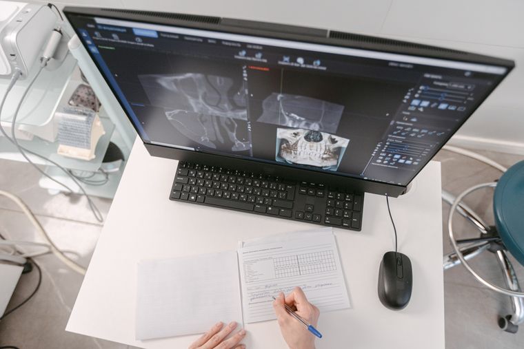 Radiologist analyzing X-ray scans on a computer monitor while taking notes. Medical documents visible.