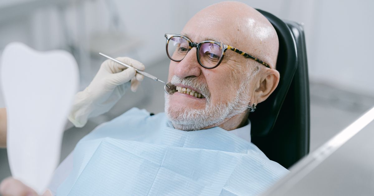 Senior man at a dental appointment examining his teeth with a hand mirror