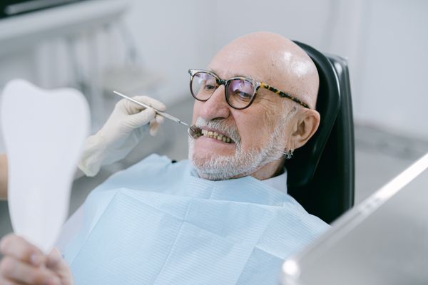 Patient checking his teeth in a mirror in the dental chair at Aurora Dental Studio