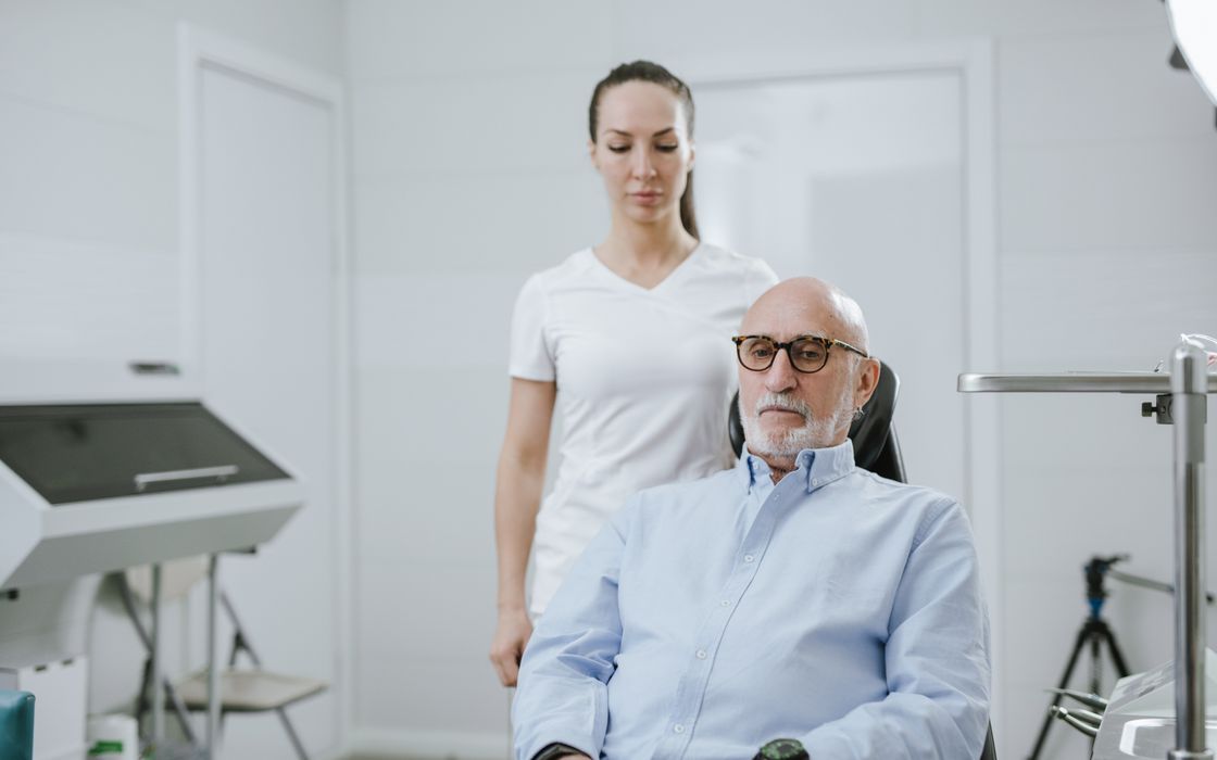 Older man seated in a clinic chair with a clinician standing behind him