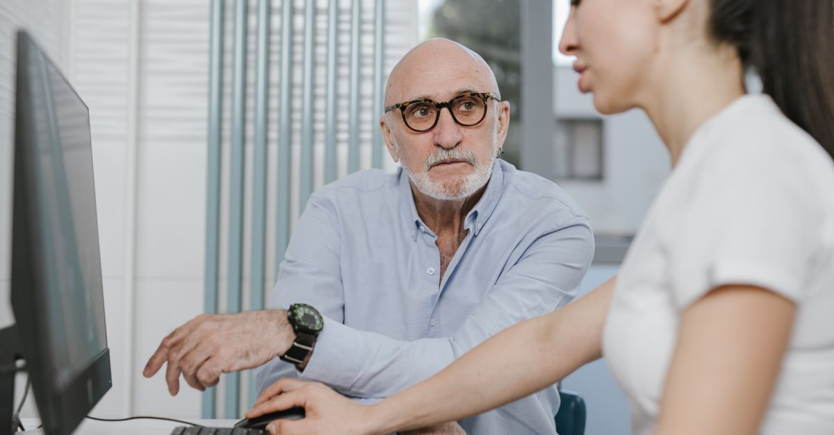 Elderly man receiving consultation from a medical practitioner in a modern indoor setting, illustrating Does Medicare Cover Eye Exams? โ 1-800-MEDIGAP, America's Trusted Toll-Free Number.