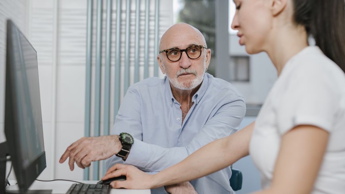 Elderly man receiving consultation from a medical practitioner in a modern indoor setting.