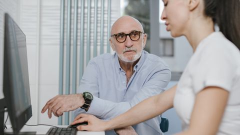 Elderly man receiving consultation from a medical practitioner in a modern indoor setting.