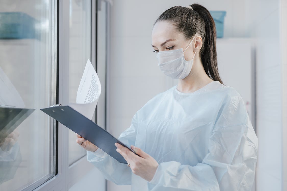 Free A female doctor in a mask examining patient's medical records in a hospital setting. Stock Photo