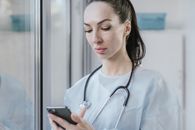 Woman in Blue Scrub Suit Holding Black Smartphone