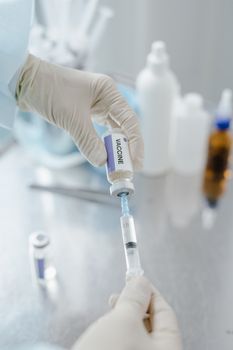 Gloved hands filling a syringe with vaccine from a vial, in a clinical setting.