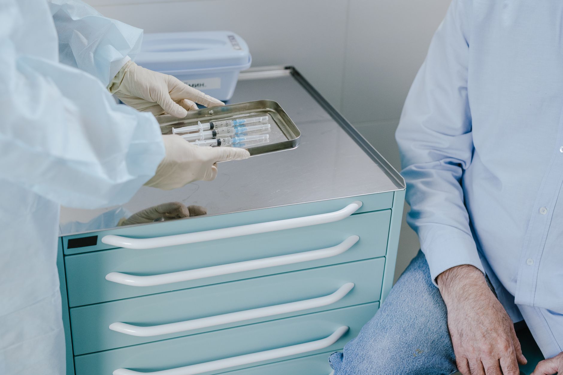 Healthcare professional handling syringes in a clinical setting with patient nearby.