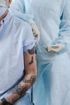 A healthcare worker in protective clothing gives an adult male a vaccine shot.