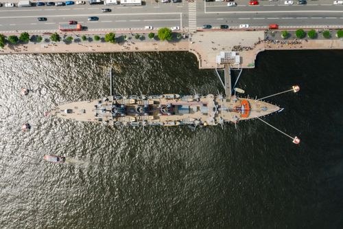 Free Top-down drone shot of a docked battleship with waterfront and adjacent road. Stock Photo