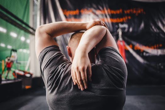Man stretching arms in a gym, viewed from behind, focusing on fitness and flexibility.