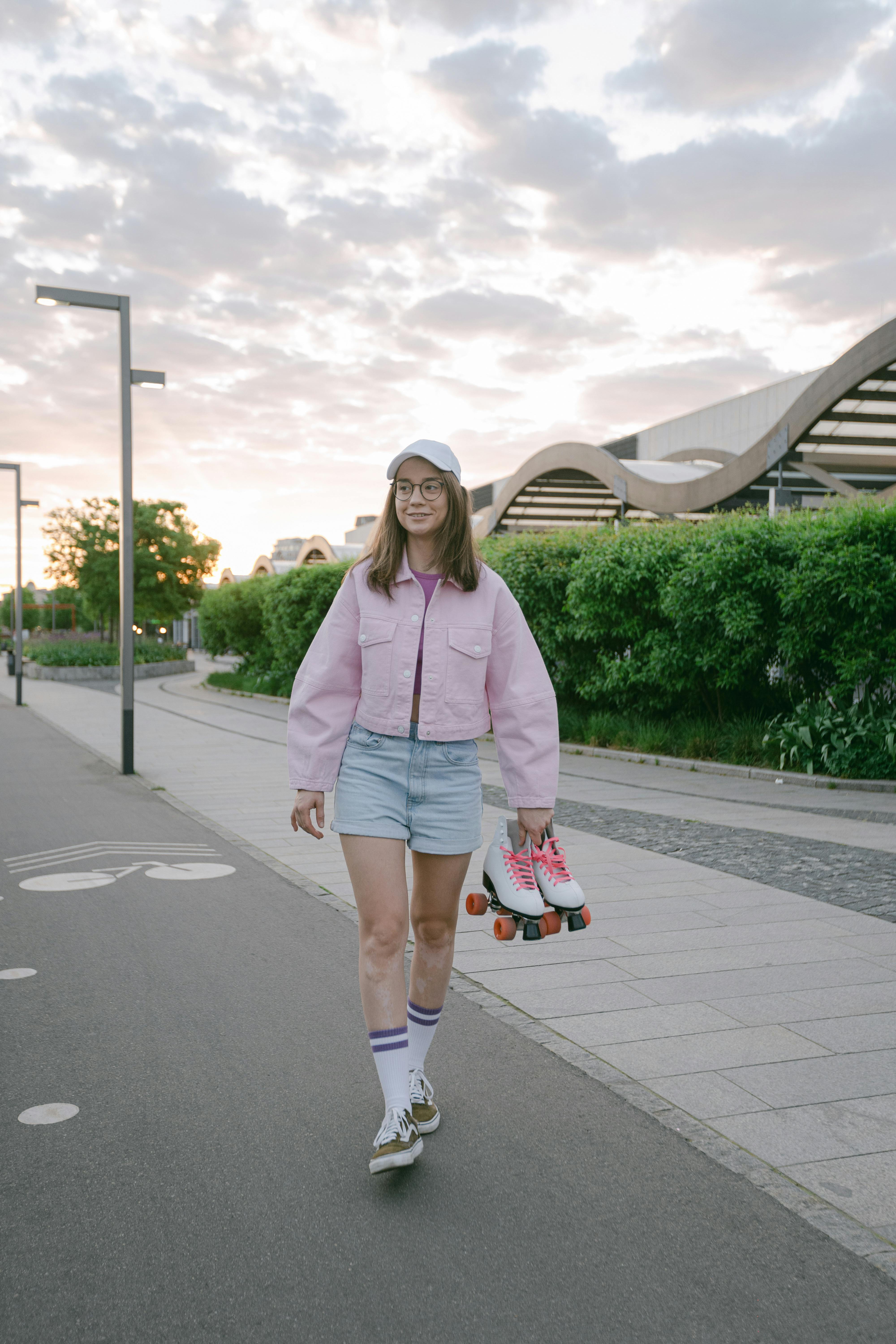 Woman in Pink Jacket and Blue Denim Shorts Standing on Gray Concrete
