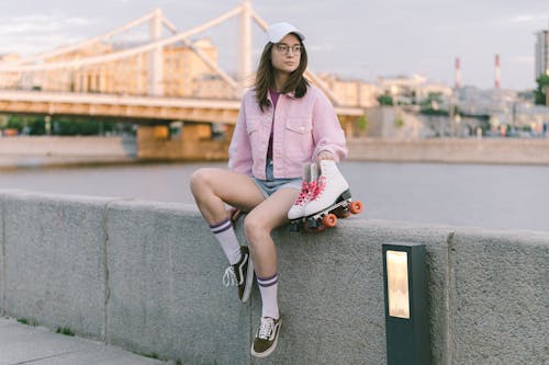 A Woman in Pink Jacket Sitting on a Concrete Bench while Holding a Roller Skates