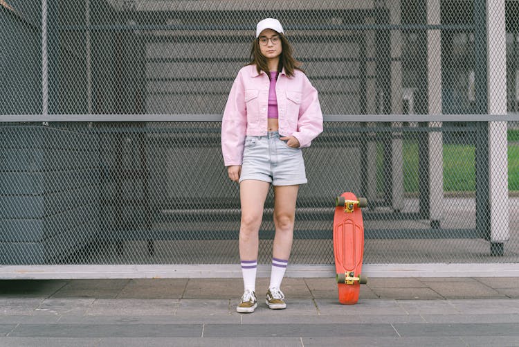 Stylish Young Woman Standing Beside A Skateboard 