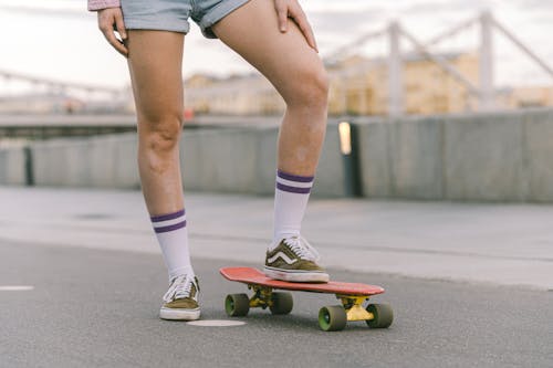 Free A Person in Denim Shorts Standing on the Street while Stepping on the Skateboard Stock Photo