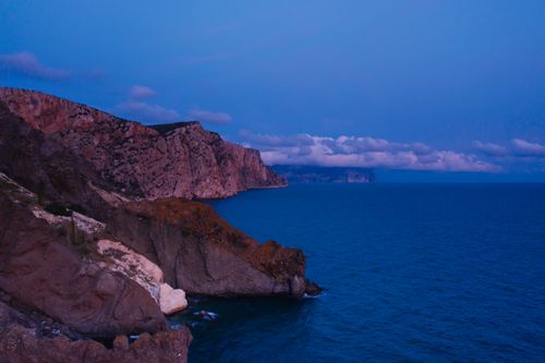 Free Stunning twilight aerial view of rocky cliffs meeting the sea under a serene blue sky. Stock Photo