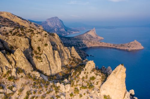 Free A breathtaking aerial view of a rugged coastal landscape with rocky hills and serene waters. Stock Photo