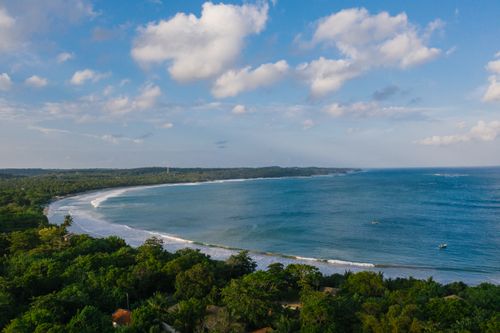 Free A breathtaking aerial view of a picturesque coastline with lush green forests and calm ocean waves. Stock Photo