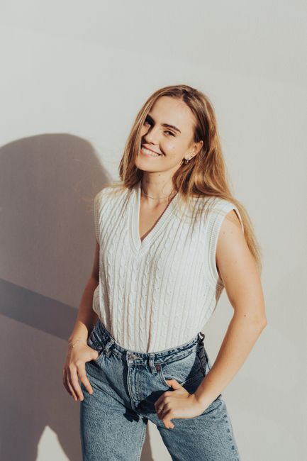 Bright portrait of a woman smiling in casual jeans and a white top, casting a shadow on a sunny day.