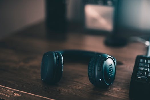Close-up of wireless headphones placed on a wooden desk in dim lighting.
