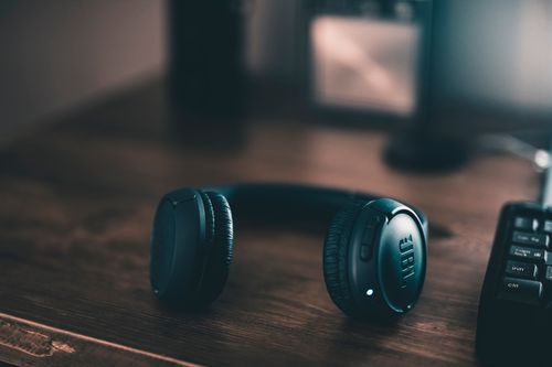 Free Close-up of wireless headphones placed on a wooden desk in dim lighting. Stock Photo