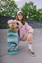 A Woman in a Pink Jacket and Denim Shorts with Her Skateboard