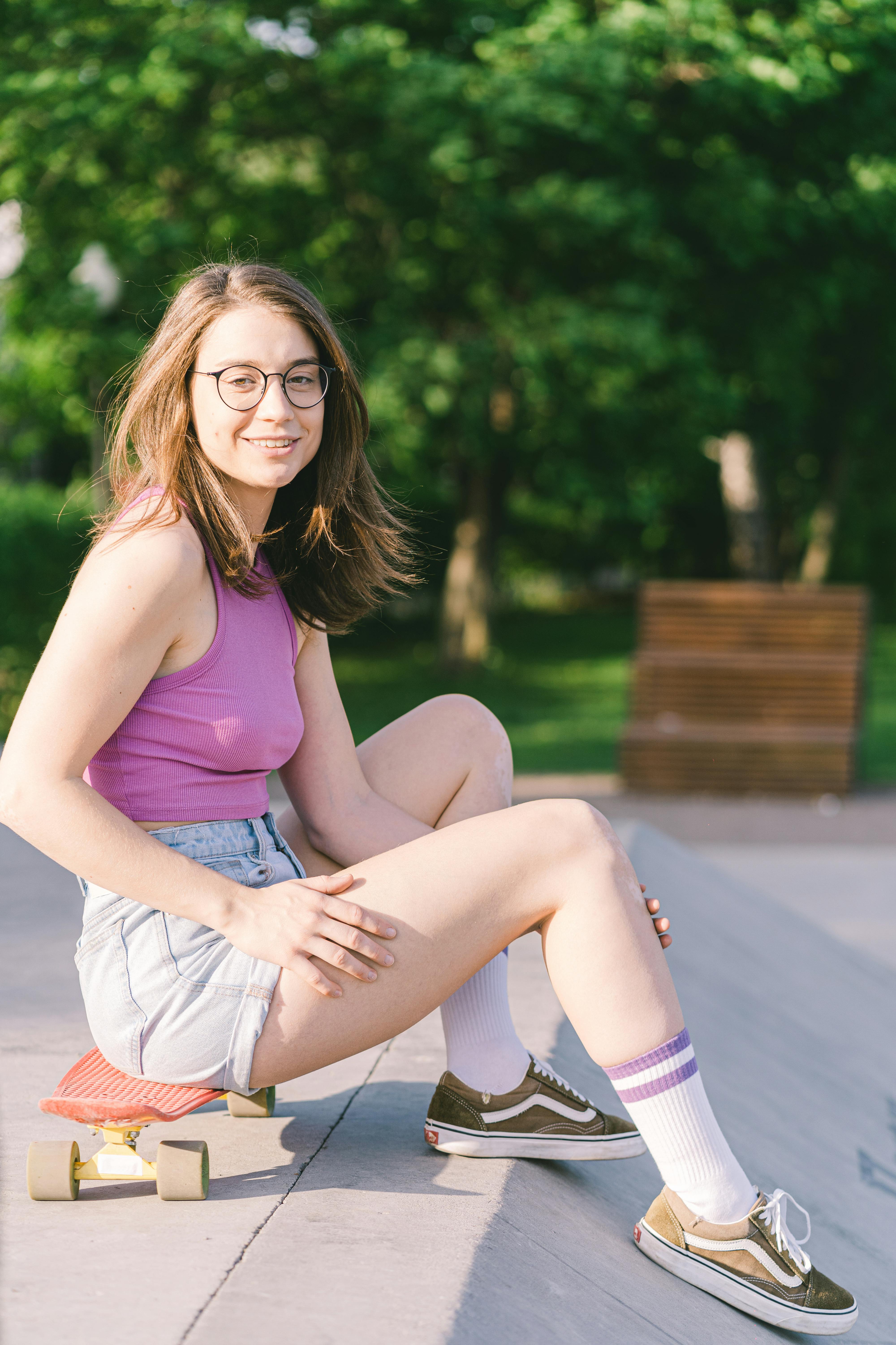 坐在公园里滑板上的一名身穿紫色背心和牛仔短裤的微笑女子