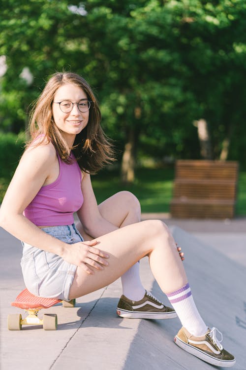 A Woman in Purple Tank Top Sitting on Her Skateboard