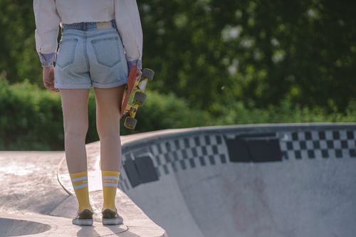 Free A back view of a young woman holding a skateboard, standing by a skate park bowl outdoors. Stock Photo
