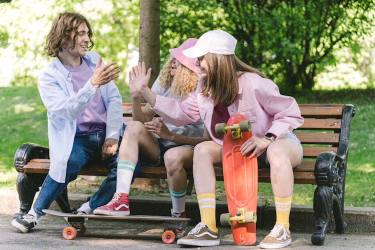 Smiling Friends Sitting With Skateboards In Park