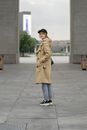 Woman in Brown Coat and Blue Denim Jeans Standing on Gray Concrete Floor