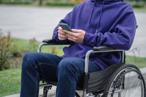 Free Person in Purple Hoodie and Blue Denim Jeans Sitting on Black Wheel Chair Stock Photo